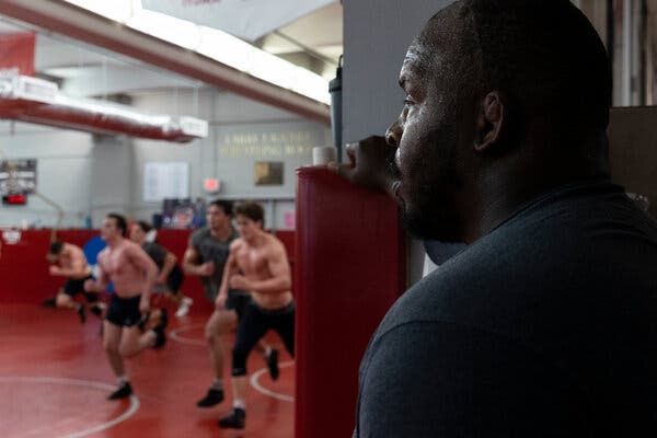 Richard Perry, in a blue shirt, watching wrestlers running in a gym.
