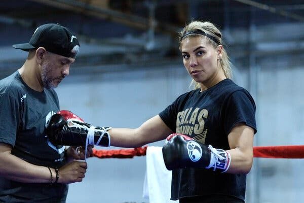 Maricela Cornejo stands in a ring while a man next to her ties on her right boxing glove.
