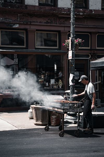 A man is cooking food on a grill in front of a building · Free Stock Photo