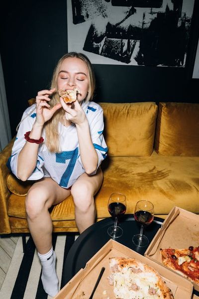 Young Woman Sitting on a Yellow Sofa While Eating Her Pizza · Free Stock Photo