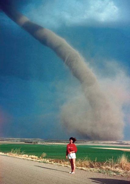 Audra Thomas posing in front of an F1 tornado swirling a mile away from her family farm (in the bac…
