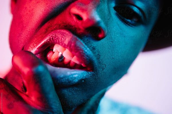 Close up shot of a man showing his gold tooth under strong pink and blue lighting