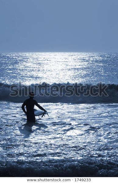 A surfer wading into the ocean waves under the moonlight.  Shot on location at Ocean City, MD, USA.