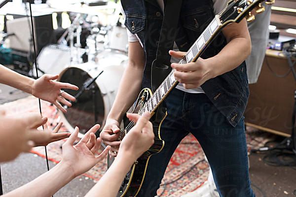 Anonymous performer playing electric guitar with fans hands by Natalie JEFFCOTTfor Stocksy United