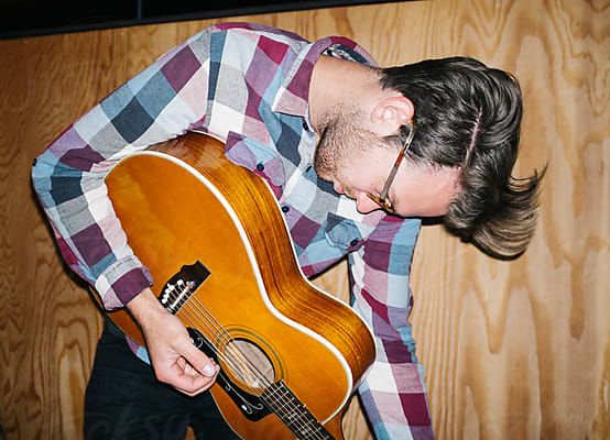 Young man plays guitar indoors by Jesse Morrowfor Stocksy United