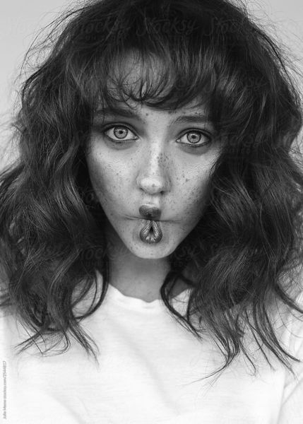 The girl with freckles makes fish lips. She wears white t-shirt and has bangs.