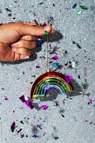 man with a shiny christmas ornament in the shape of a rainbow with confetti