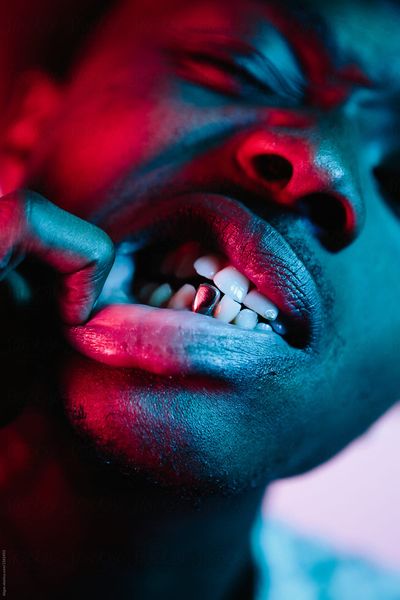 Close up shot of a man showing his gold tooth under strong pink and blue lighting