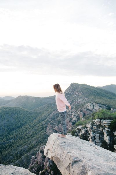 Side view of pretty woman standing with hands apart at the edge of the hill.