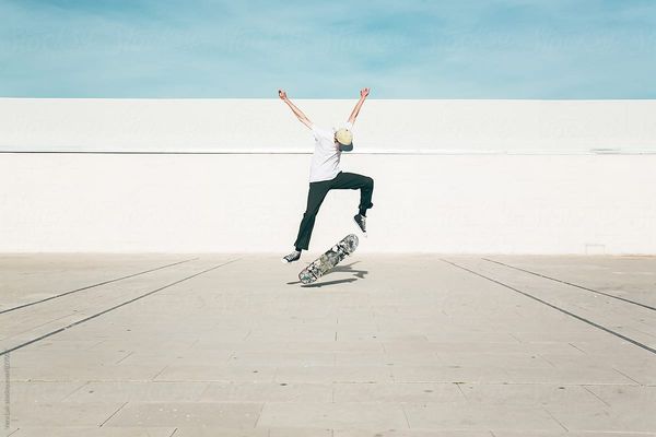 Young man performing a skate trick using his skateboard against of white wall outdoors. Summer time…