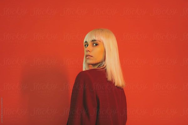 From below shot of stylish beautiful woman with white style hair wearing red jacket looking at came…
