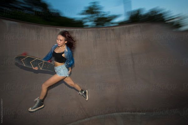 A young asian woman on a skateboard in a skatering. She is wearing shorts, sneakers and a denim shi…