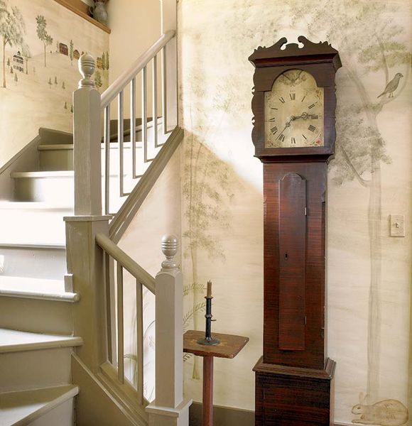 In an 1830 Greek Revival, the stair hall is painted with a mural in the manner of early American it…