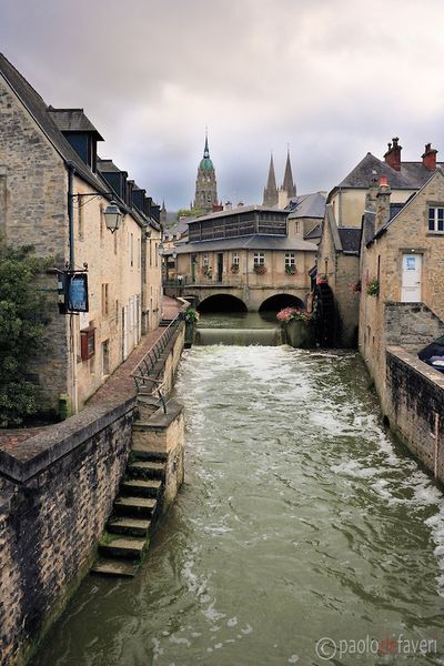 A view of downtown Bayeux, with its canals, stone buidings and cobblestone lanes, and the cathedral…