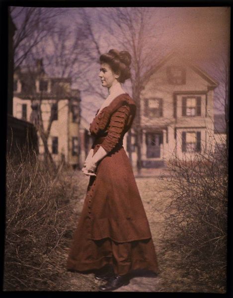 Woman wearing red dress with houses  in background, 1915 autochrome
