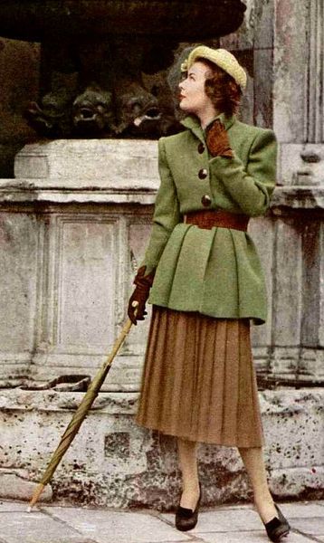 1947 Model is wearing a long moss-green belted jacket over brown pleated skirt by Jacques Fath!